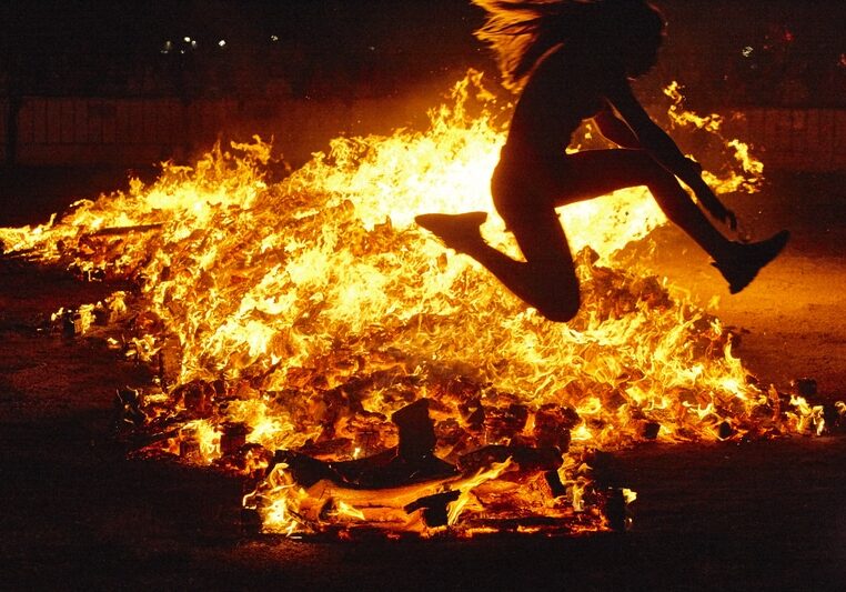 Summer solstice celebration in Spain. Woman jump. Fire flames. Horizontal